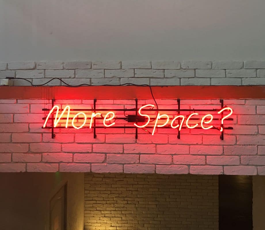 Rote Leuchtschrift More Space? auf einer Backsteinwand